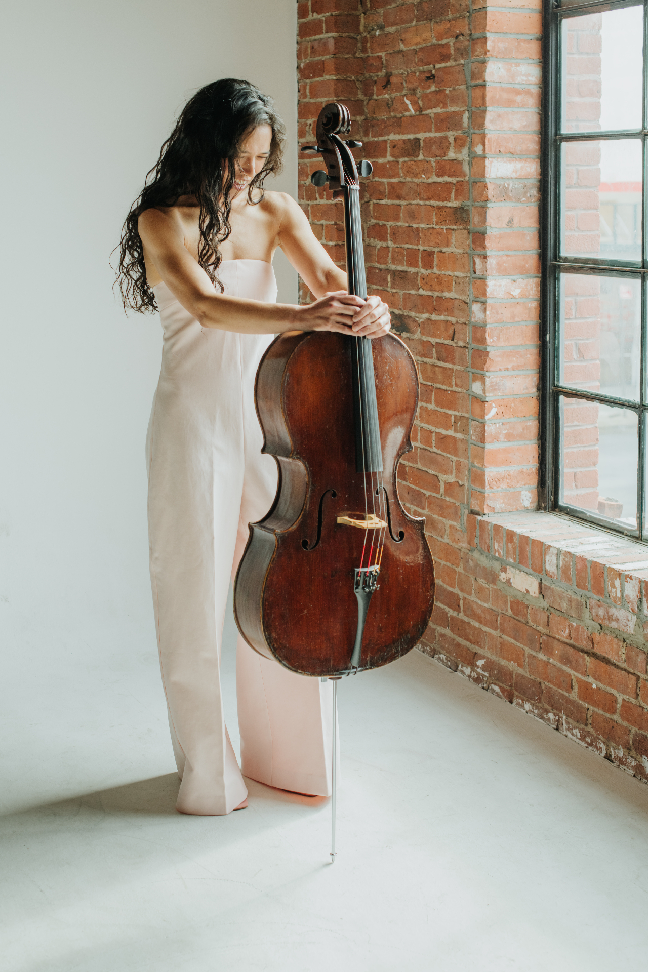 Paloma Ferrante with cello beside a brick brownstone window